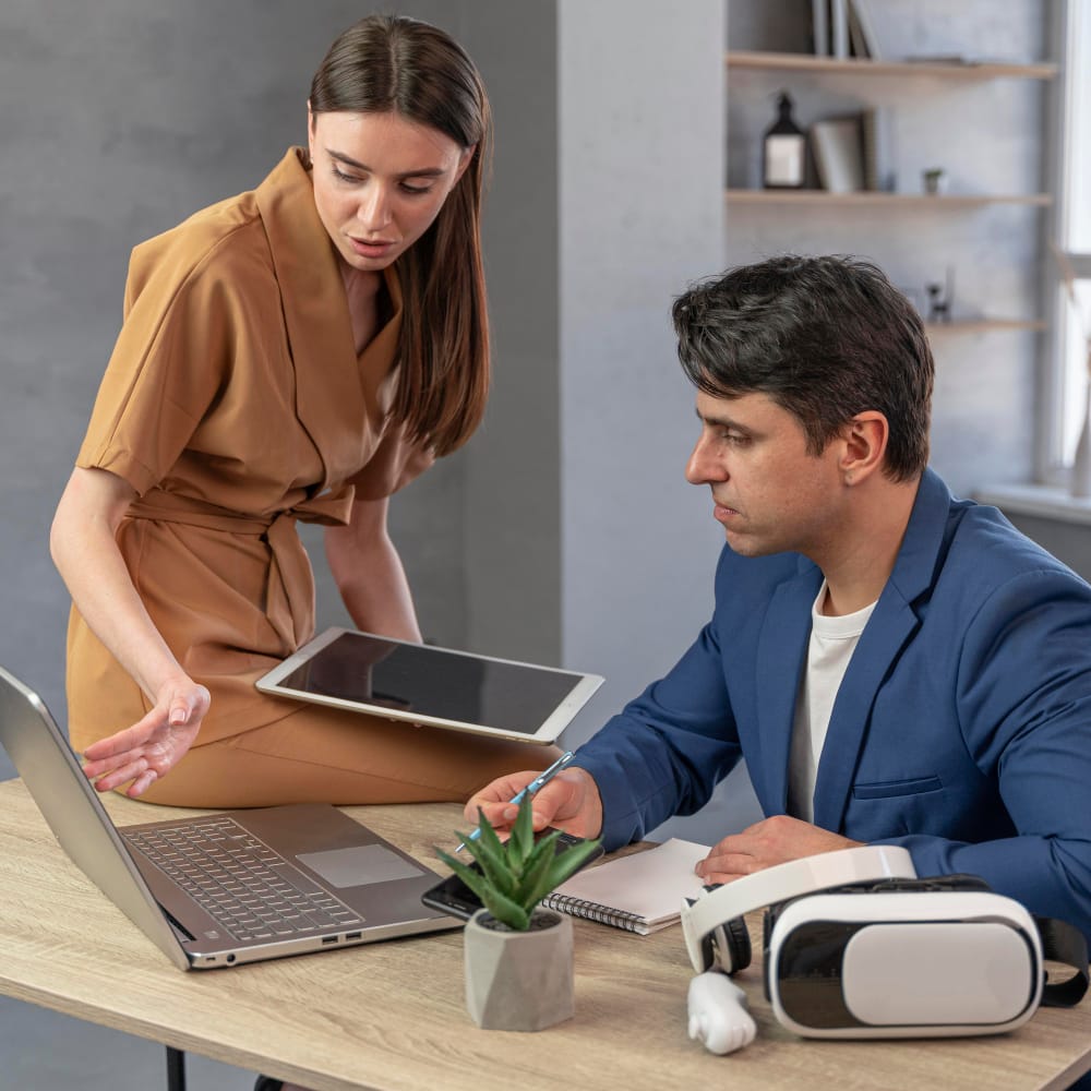 Two real estate professionals use a laptop, tablet, and AI-powered headset showing how to run comps and analyze property data in a modern office setting.