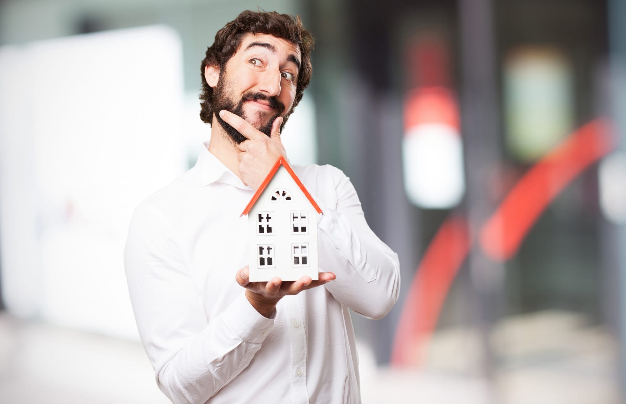 Man in a white shirt holding a small model house and smiling thoughtfully.