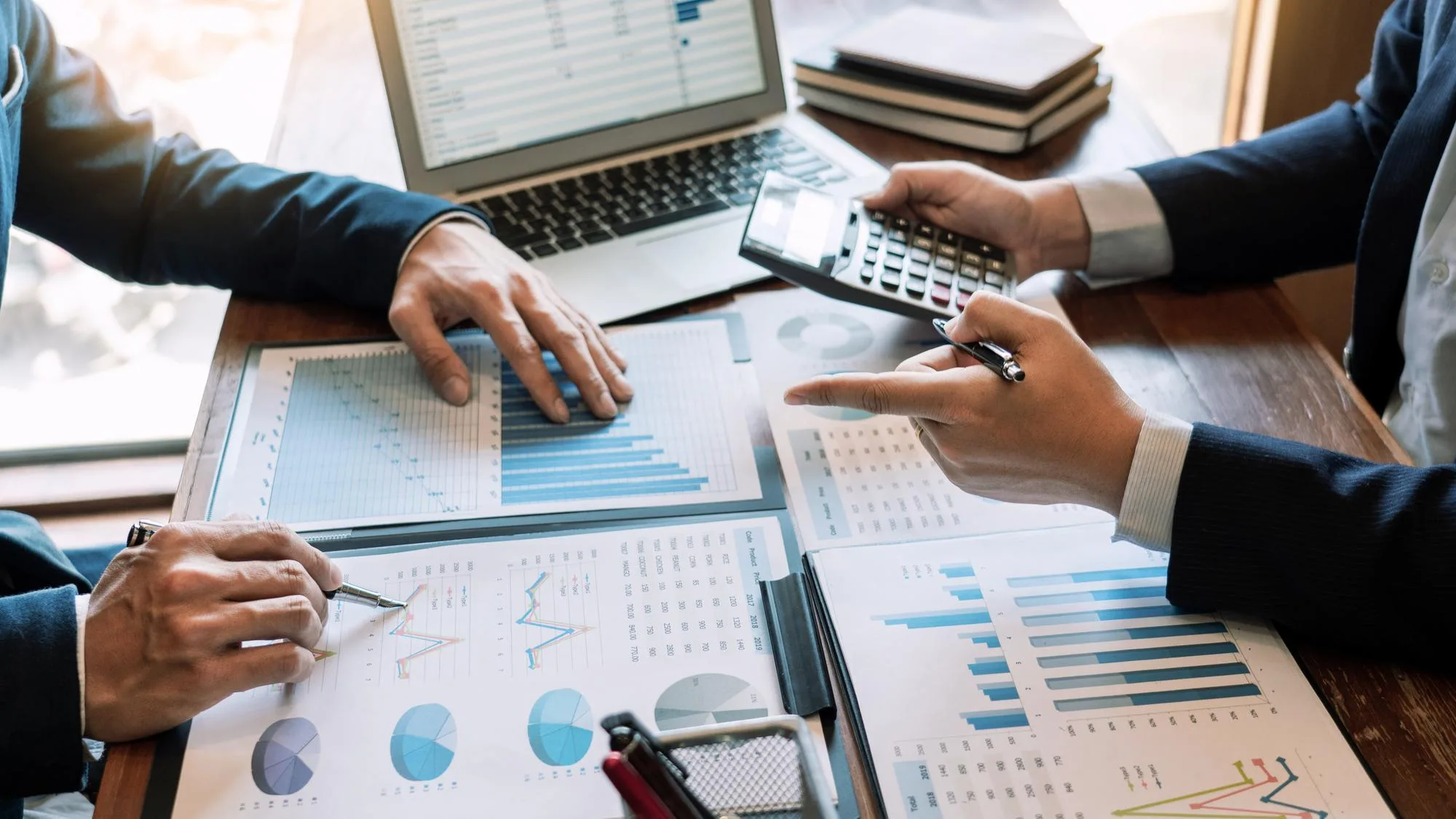 Two investors using financial charts, a laptop and a calculator to analyse an investment property