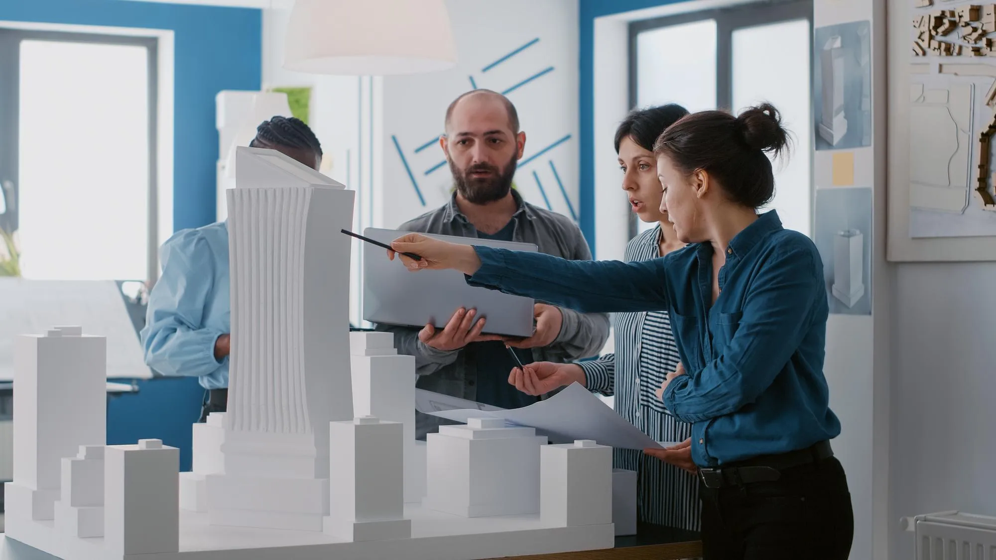 Professionals in a real estate development office analyze an architectural model, planning the financial viability of a project that will be funded by a large-scale mortgage.