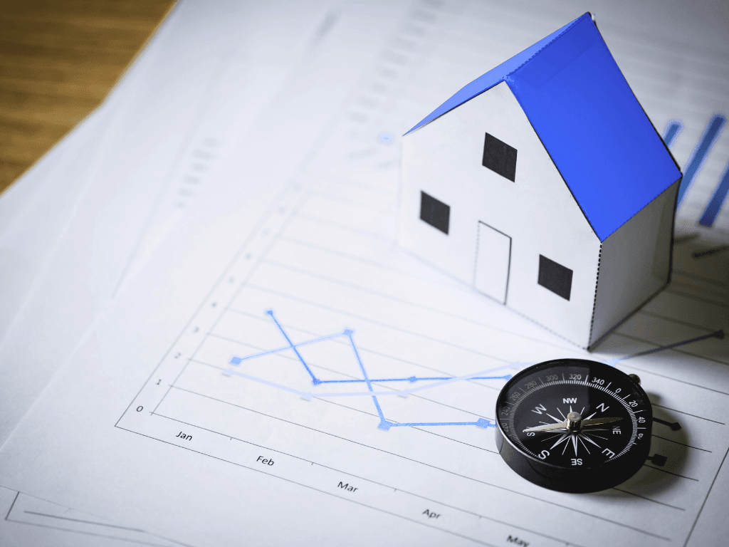 Paper house model and compass on financial charts, symbolizing data-driven real estate investing direction and strategy in the US housing market