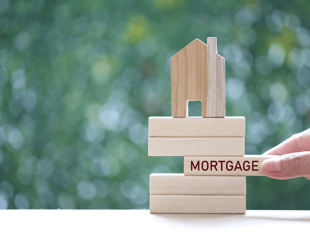 6 Best AI Real Estate Analytics Tools 3 Hand pulling a wooden block labeled ‘mortgage’ from a stacked wooden house model, symbolizing Real Estate Analytics Tools