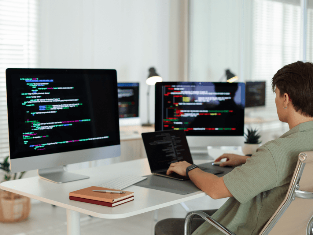 Software developer coding at multiple monitors while working on backend services for a modern real estate app