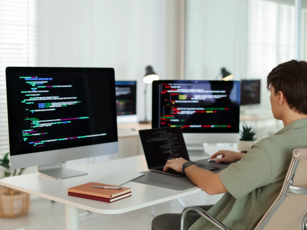 Software developer coding at multiple monitors while working on backend services for a modern real estate app