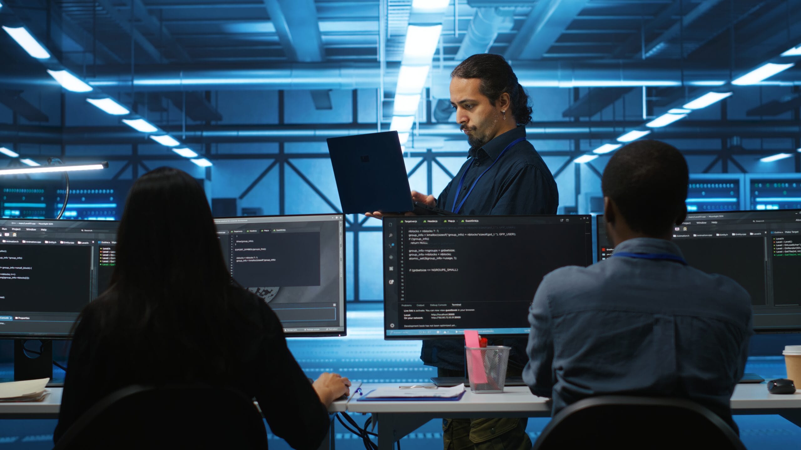 IT developers reviewing real estate API integration code on multiple monitors in a server room