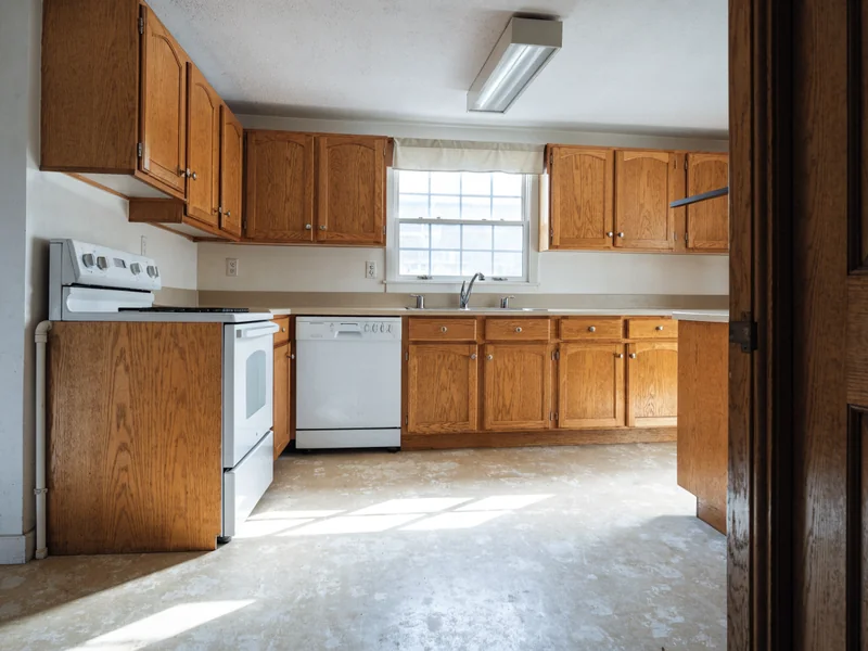 Kitchen with worn oak cabinets, old appliances and stained flooring