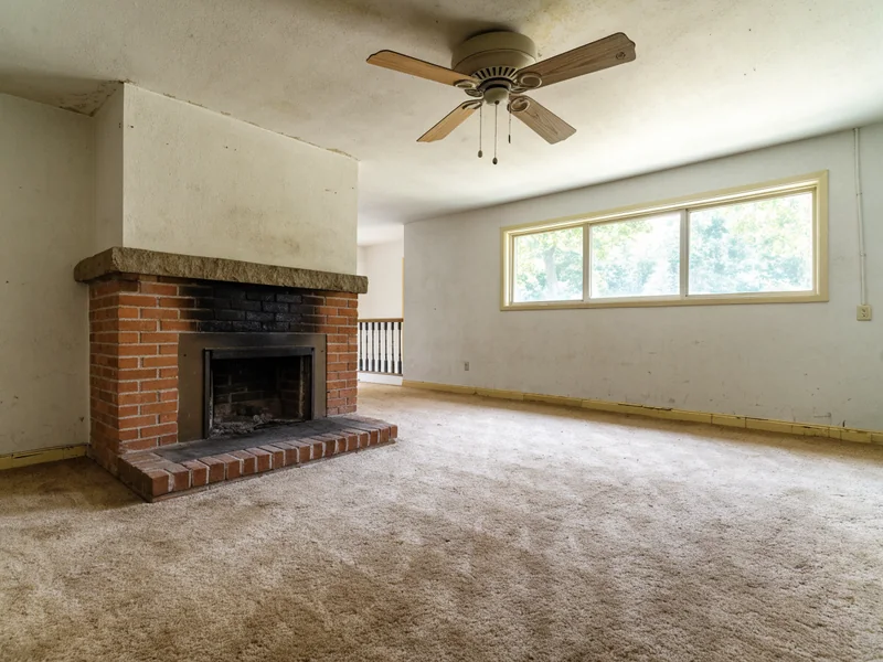 Living room with a brick fireplace and worn carpet